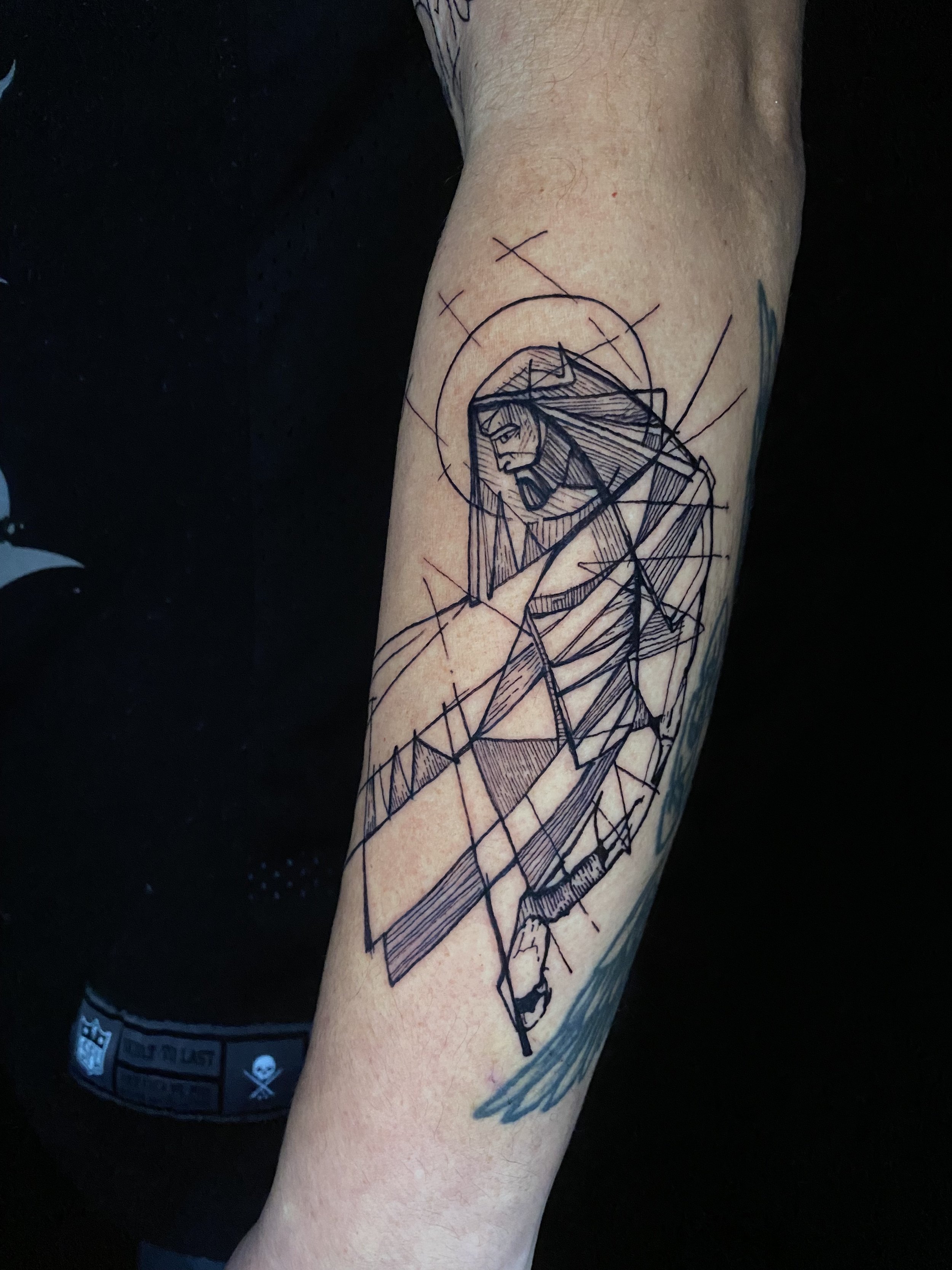 Tattoo of a stylized face with a beard and hair, designed with geometric lines, on a person's forearm.