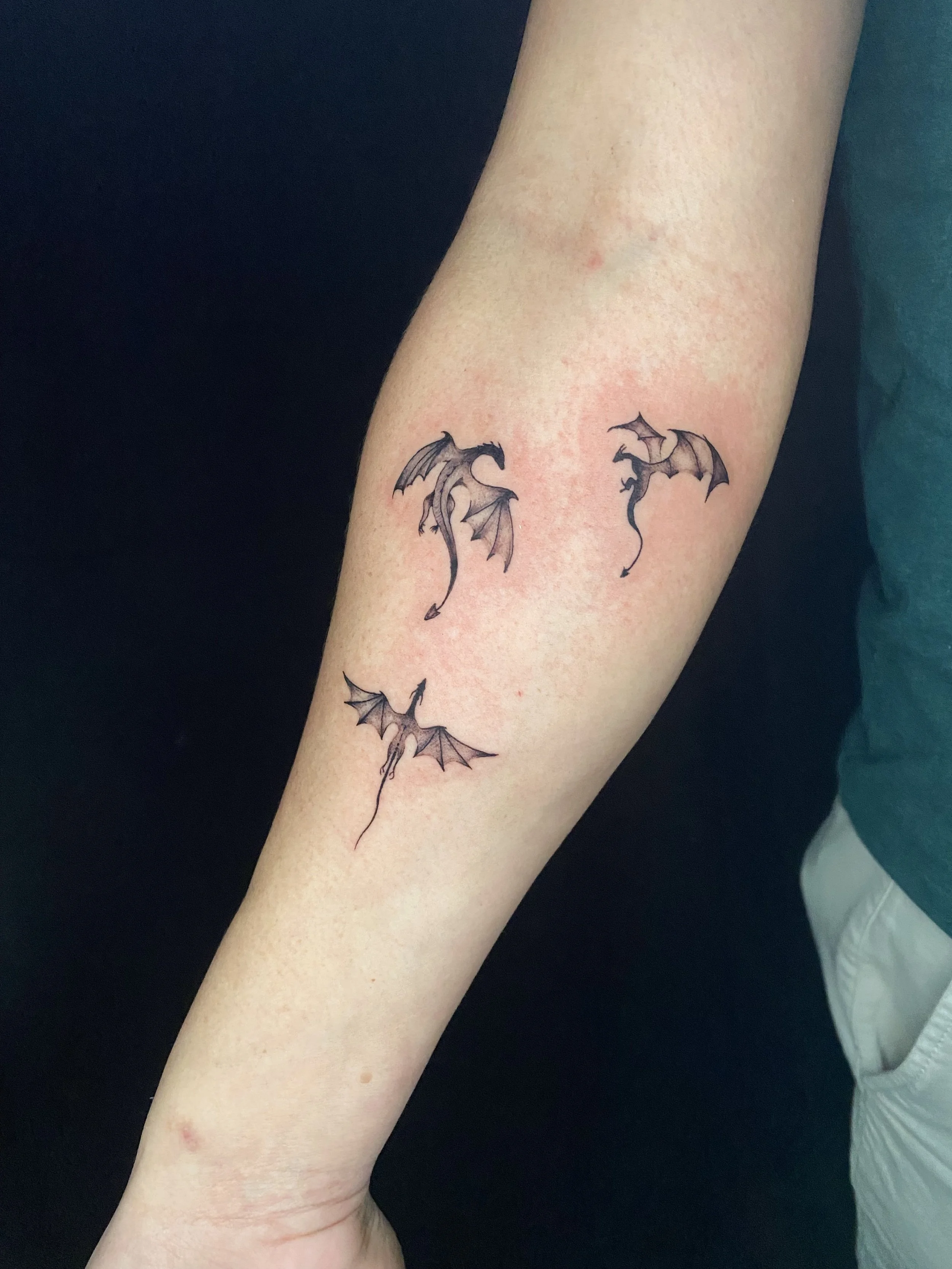A person's forearm with a tattoo of three small bats flying, each with outstretched wings, in black ink.