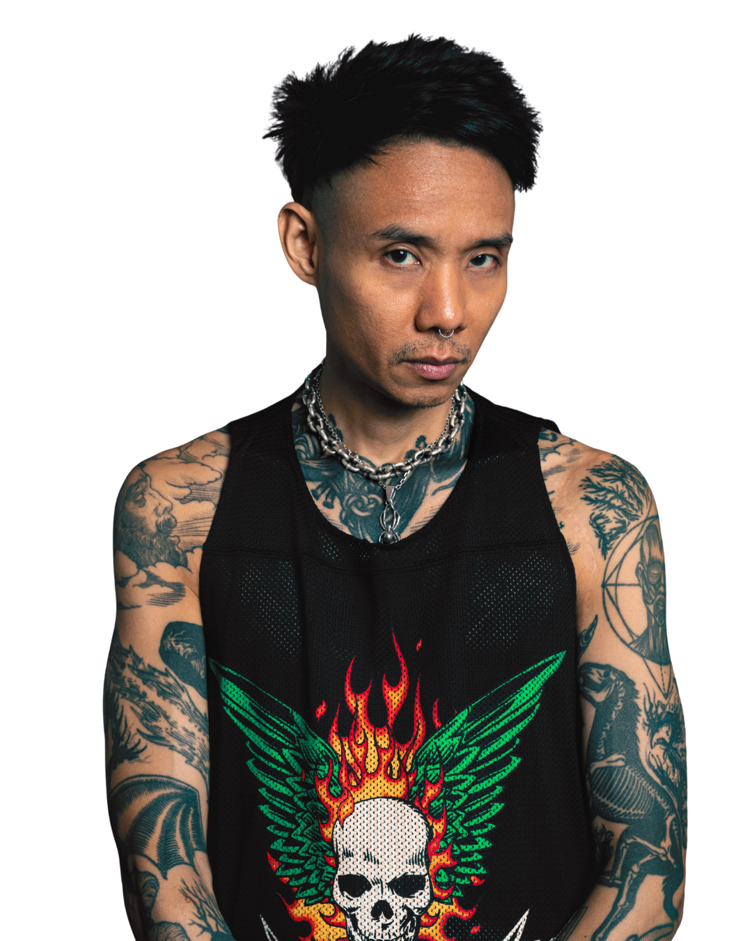 A young man with tattoos on his arms and chest, wearing a black sleeveless shirt with a colorful skull and flames design, and layered silver necklaces.