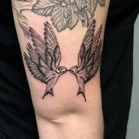 Tattoo of a bird with outstretched wings holding a ring in its beak on a person's arm