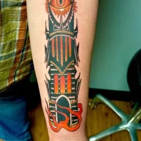 A tattoo of a stylized insect with a red, orange, and green color scheme on a person's forearm.