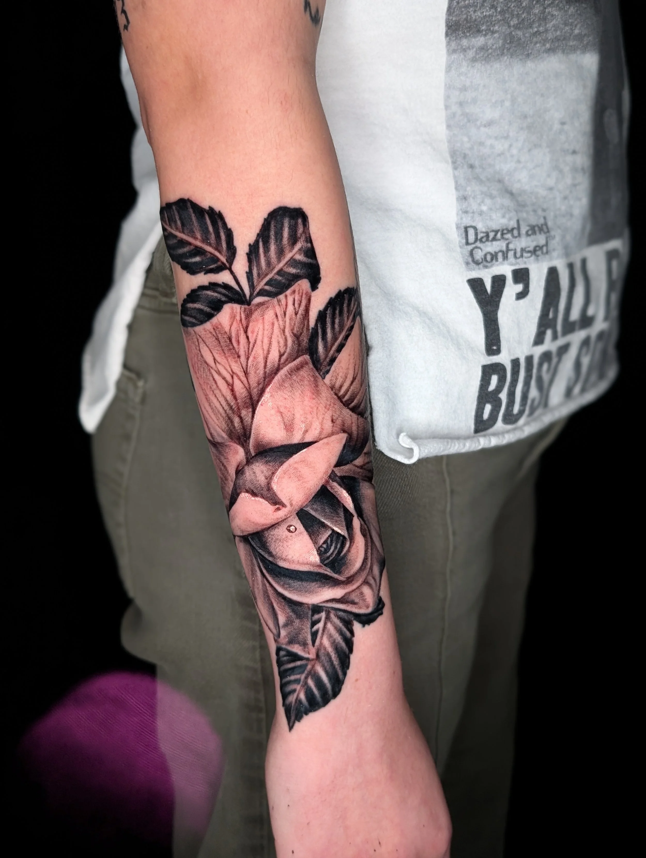 Close-up of a person's arm with a detailed black and gray tattoo of a rose with leaves.