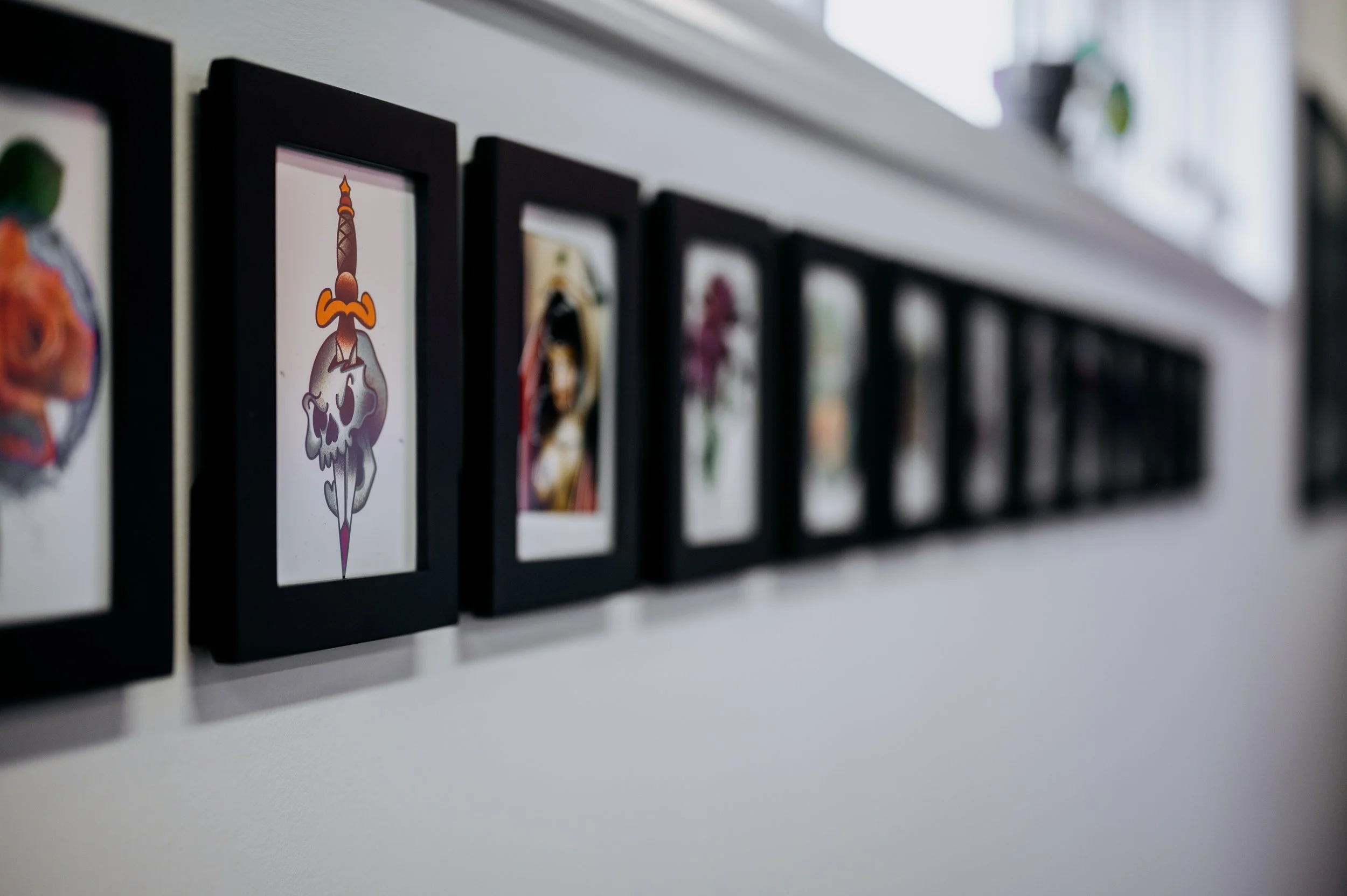 Close-up of framed artwork on a white shelf, featuring a stylized skull with a tattooed skull and a sword growing from the top.