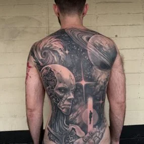 A man with a large back tattoo featuring a female face, planets, stars, and cosmic themes.