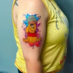 Colorful tattoo of a bear wearing a hat and sunglasses on a person's upper arm.
