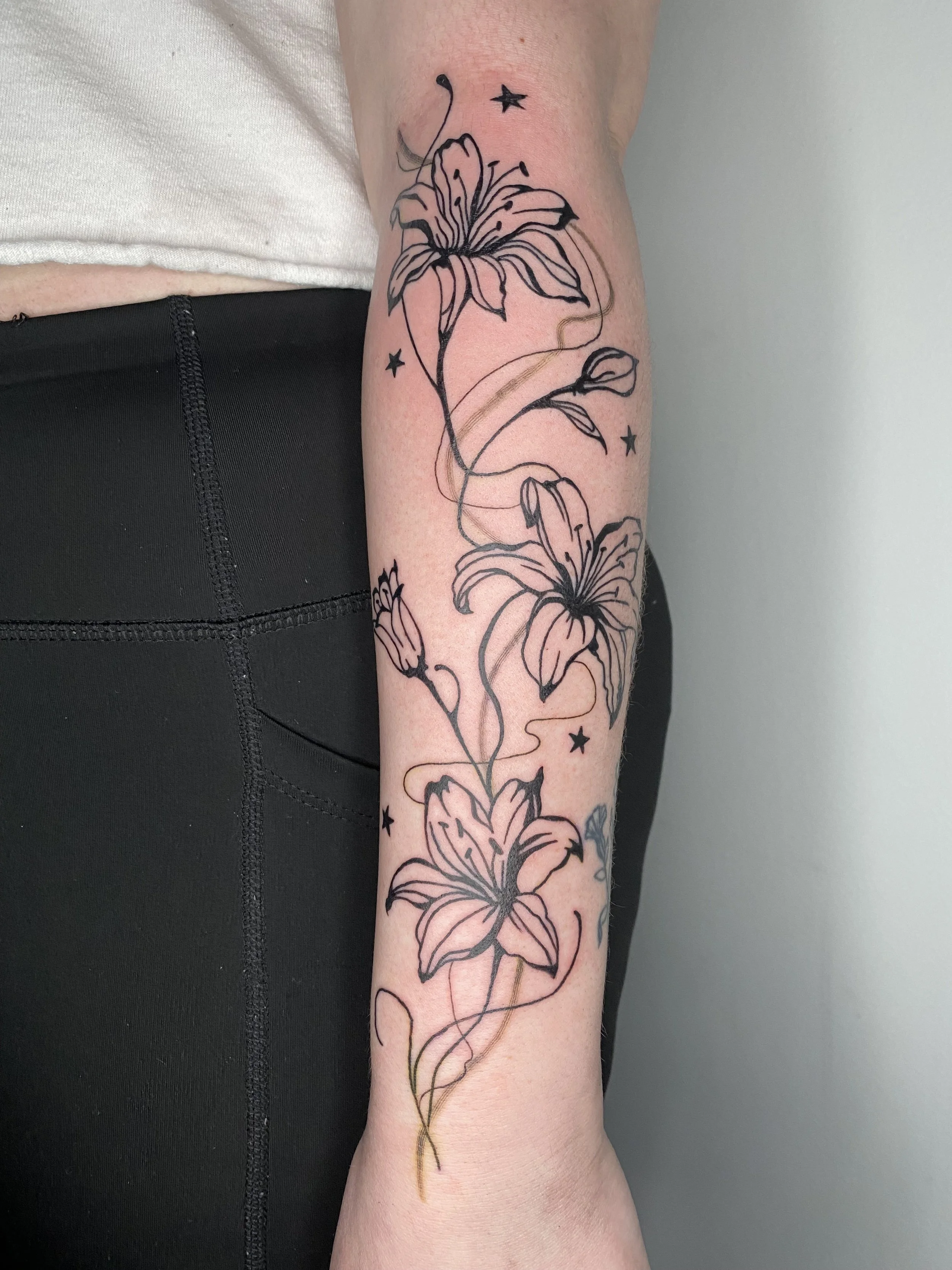 A tattoo of a lily flower with stars and flowing lines on a person's forearm.
