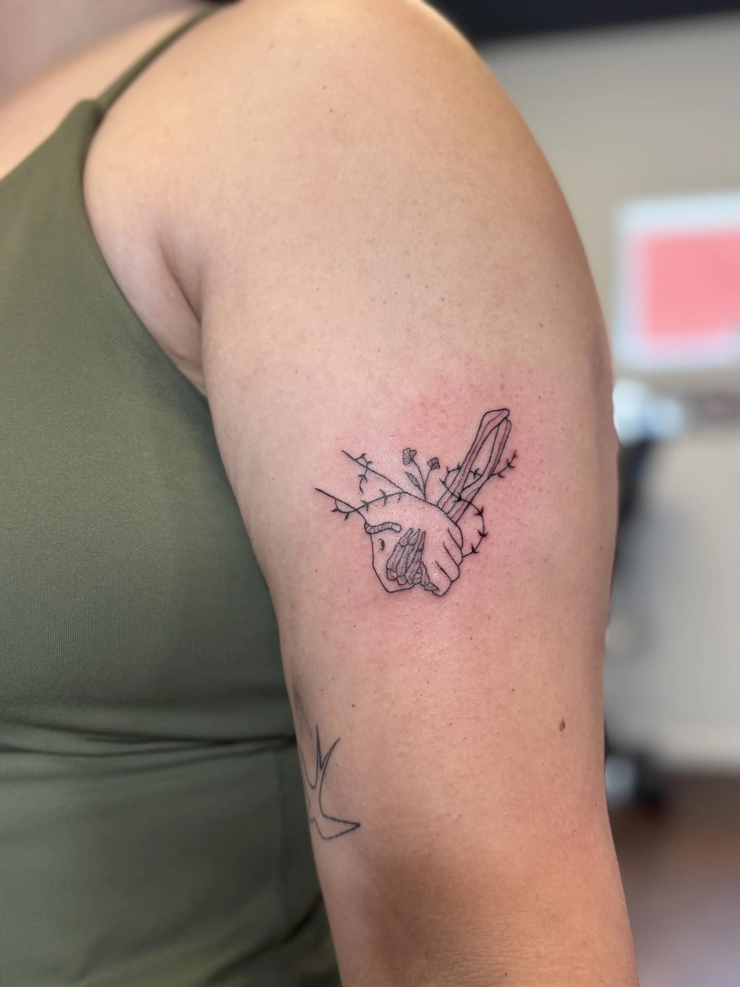 A tattoo of two hands shaking with a thorny vine wrapped around the wrists, situated on a person's upper arm.