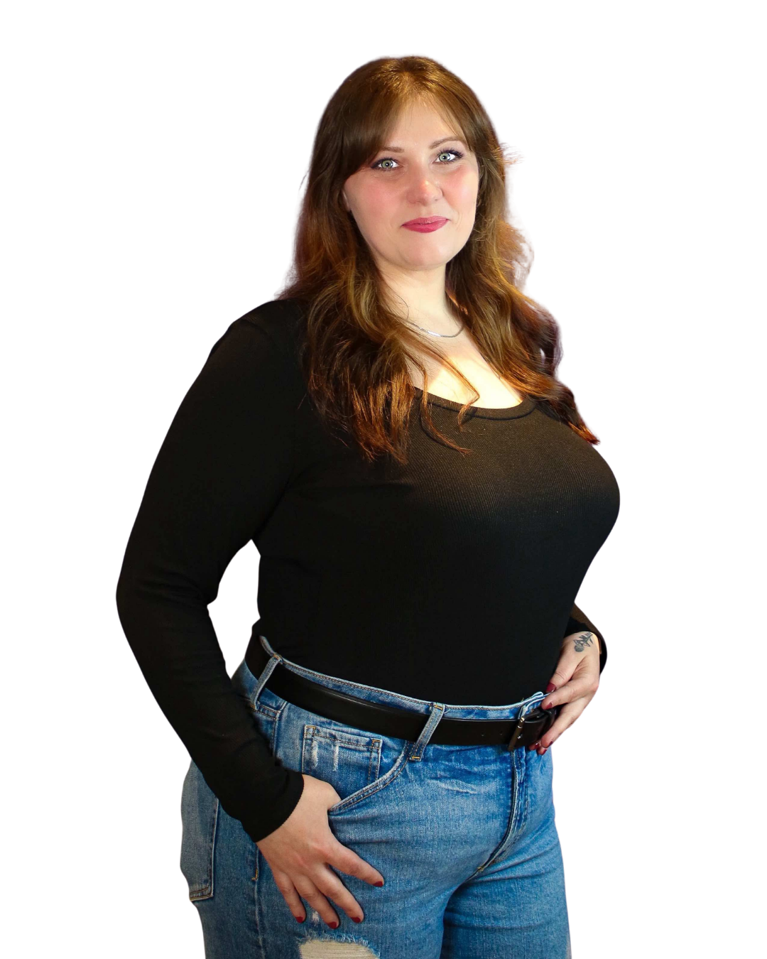 A young woman with long, wavy brown hair, wearing a black long sleeve shirt and blue jeans with a belt, standing with her right hand in her pocket and her left hand resting on her hip against a black background.