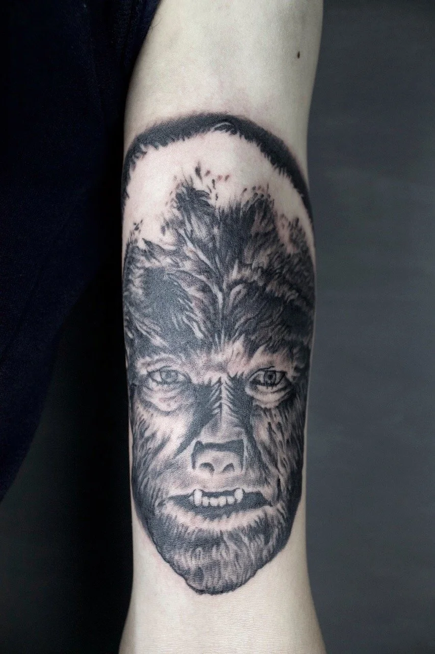 Tattoo of a werewolf face on a person's arm, with detailed fur and features.