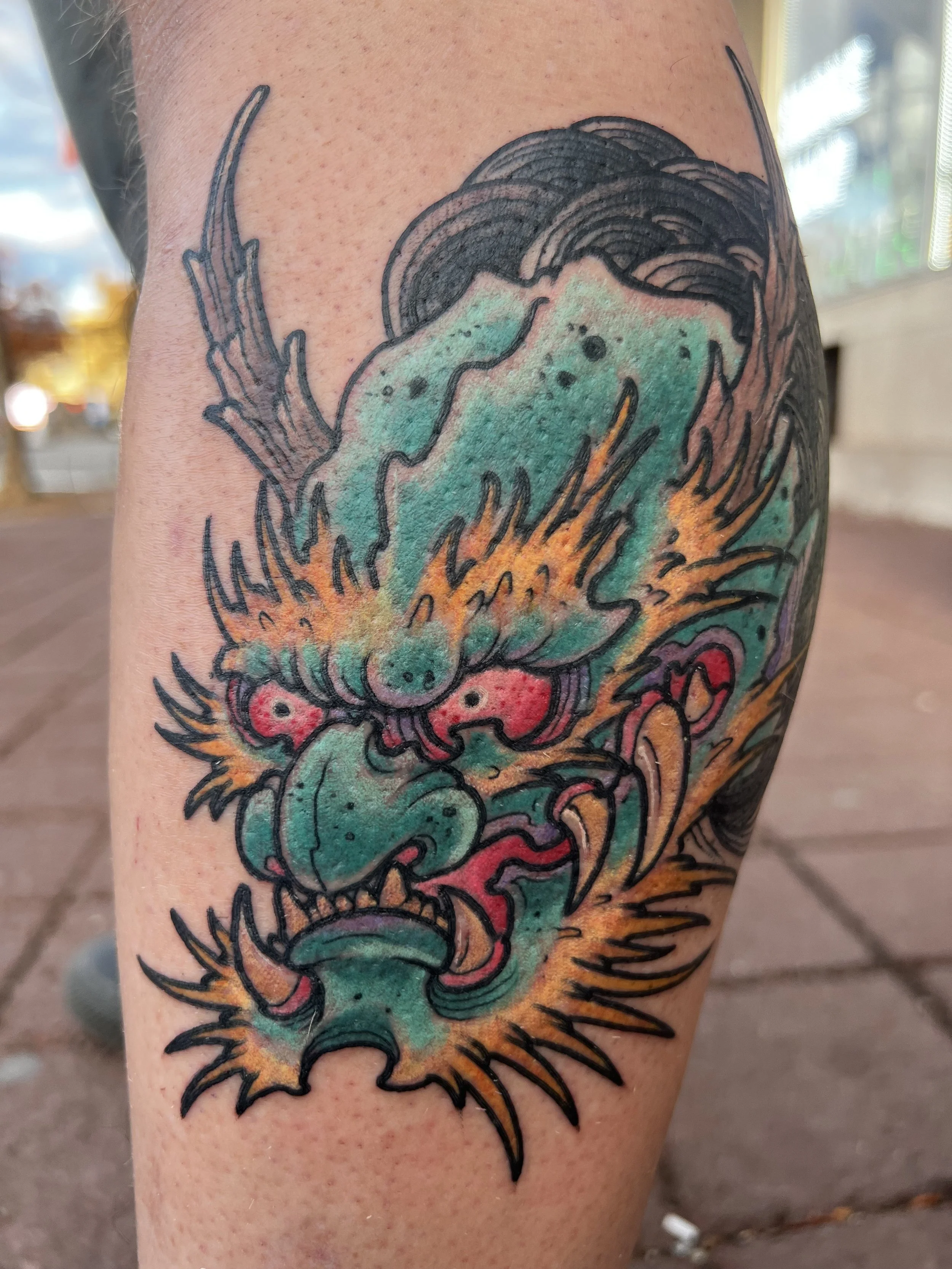 Tattoo of a colorful dragon coiled around the person's arm, with detailed scales, clouds, and fire elements in the design.