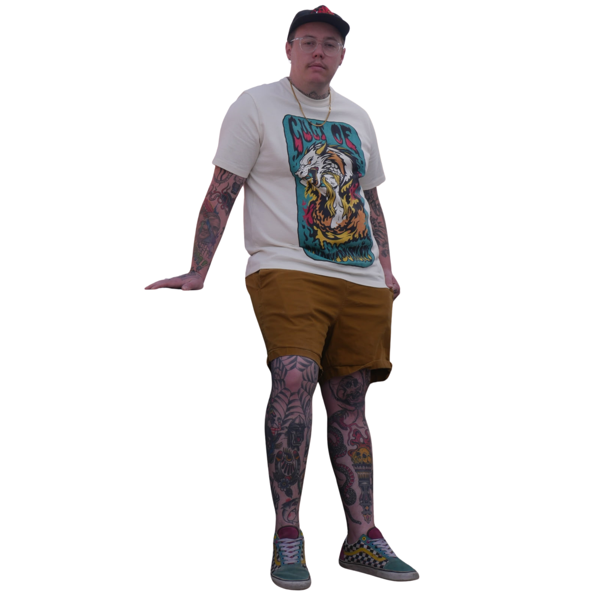 A man standing against a black background, wearing a white graphic t-shirt, brown shorts, colorful sneakers, a black cap, clear glasses, and jewelry, with visible tattoos on his arms and legs.