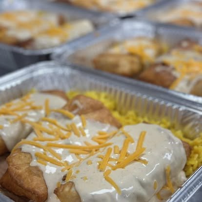 Baked chicken breasts topped with white gravy and shredded cheddar cheese in aluminum trays.