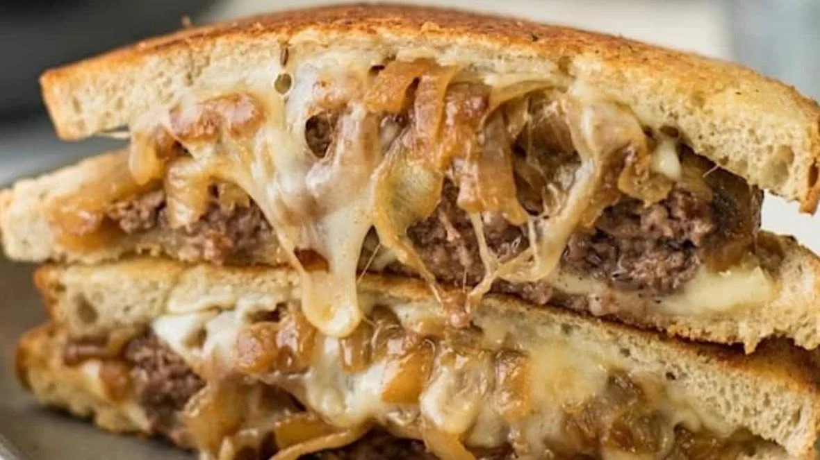 Close-up of a cheeseburger with melted cheese, grilled onions, and a beef patty inside a toasted bun.