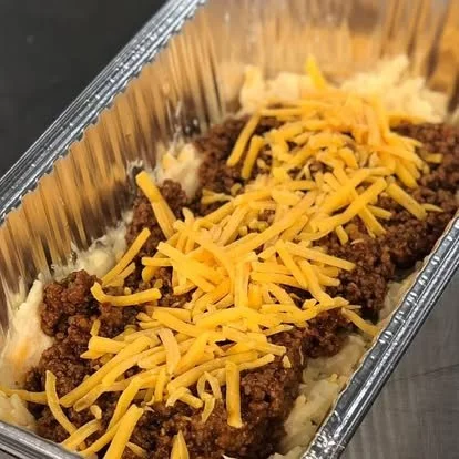 Layered taco casserole in a disposable aluminum tray topped with shredded cheddar cheese