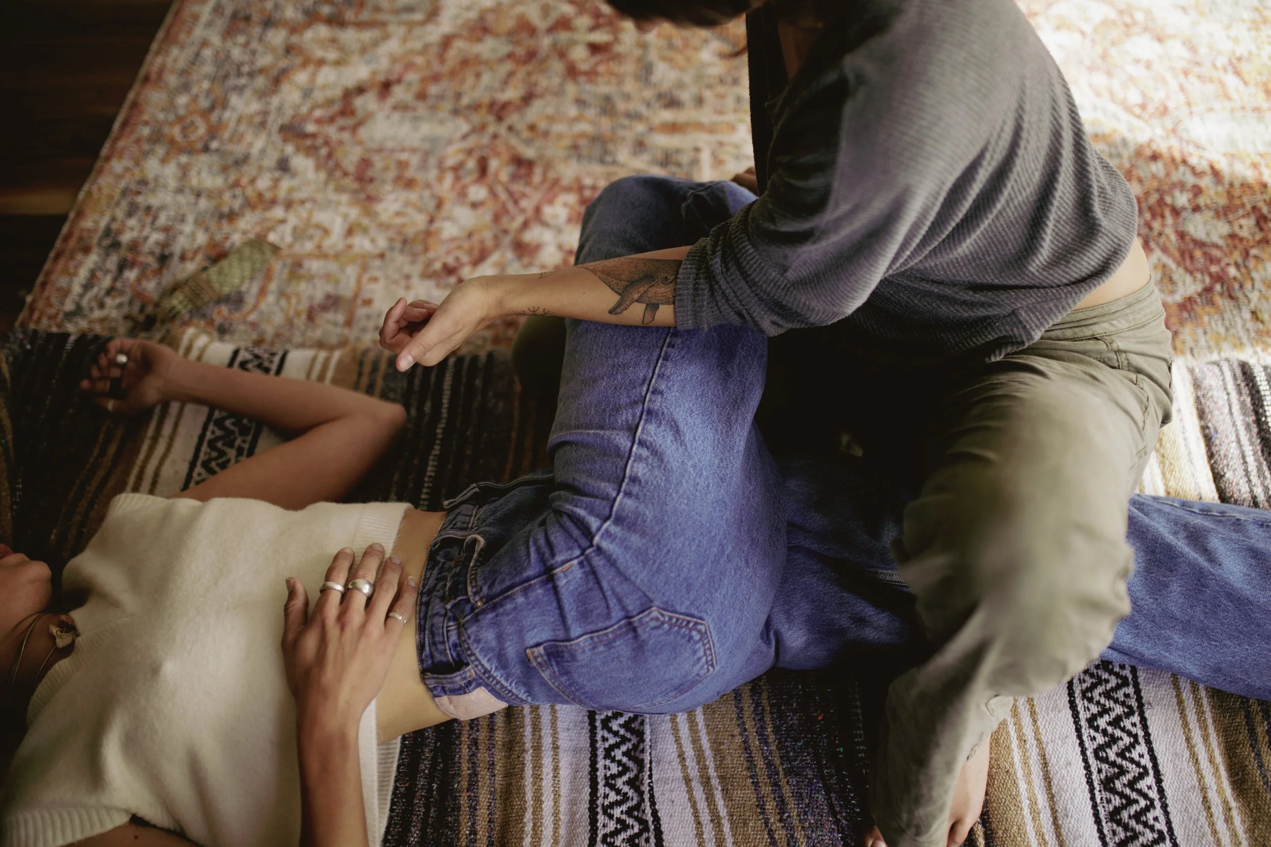 Person lying down on a patterned rug, receiving chest compressions from another person.