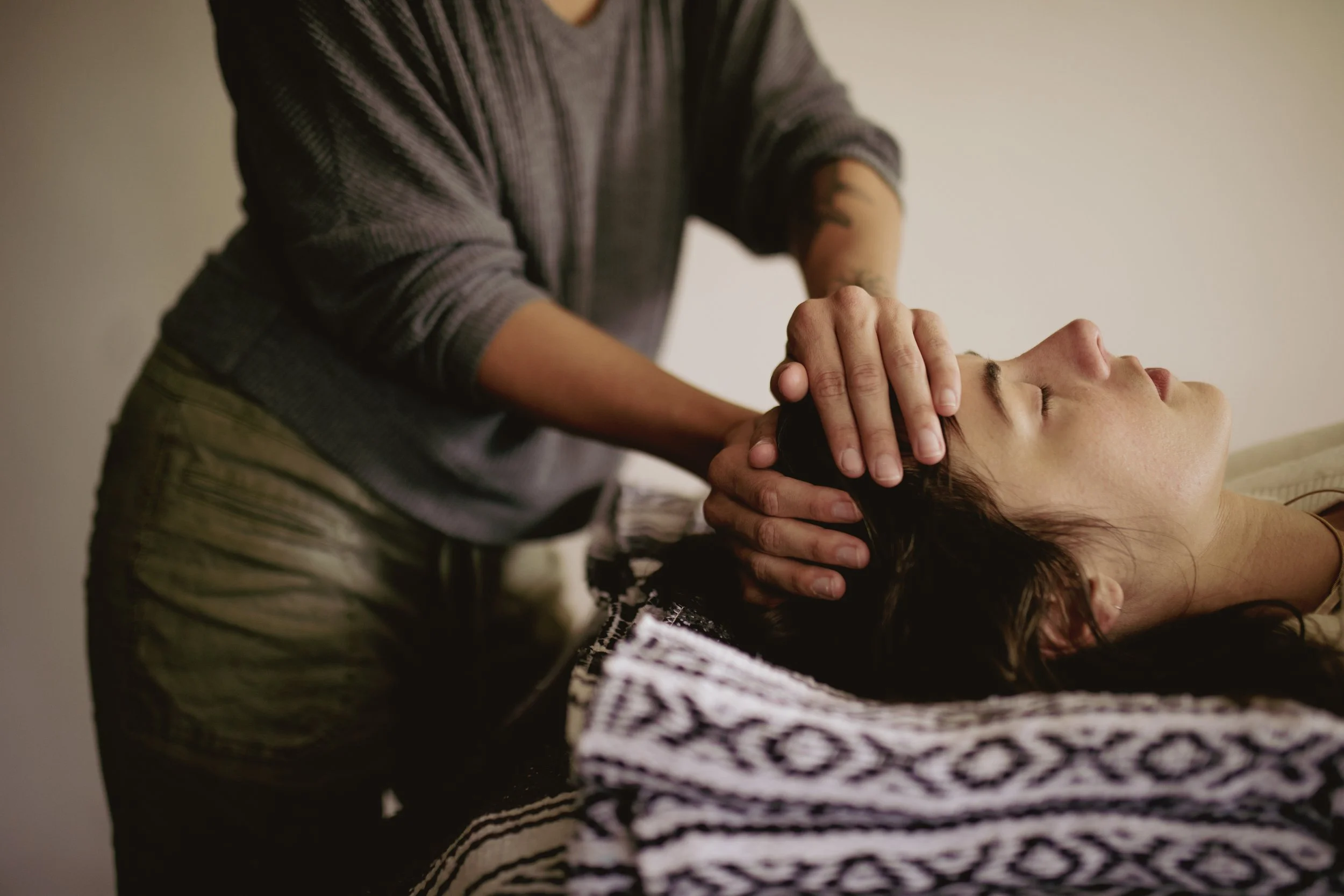 A person performing a neck massage on a woman lying down with closed eyes.