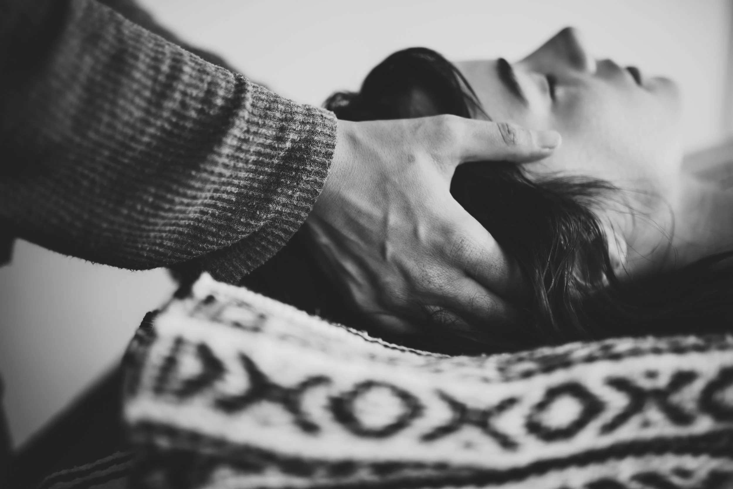 Black and white photo of a person lying down with their hand on their face, wearing a long-sleeve top, with long hair partially covering their face.
