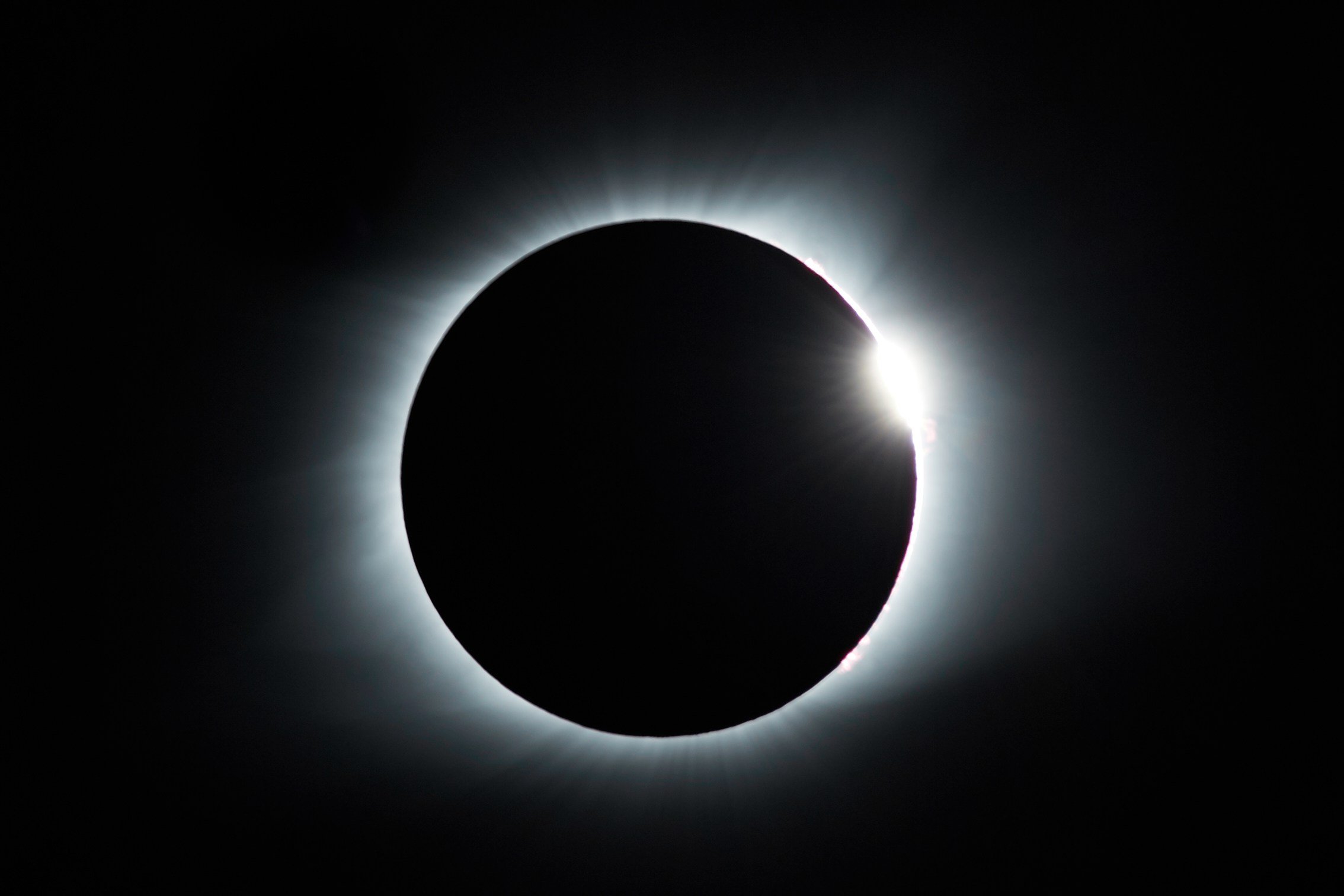 The image shows a solar eclipse where the moon is covering the sun, creating a dark circle with bright light radiating around its edges.