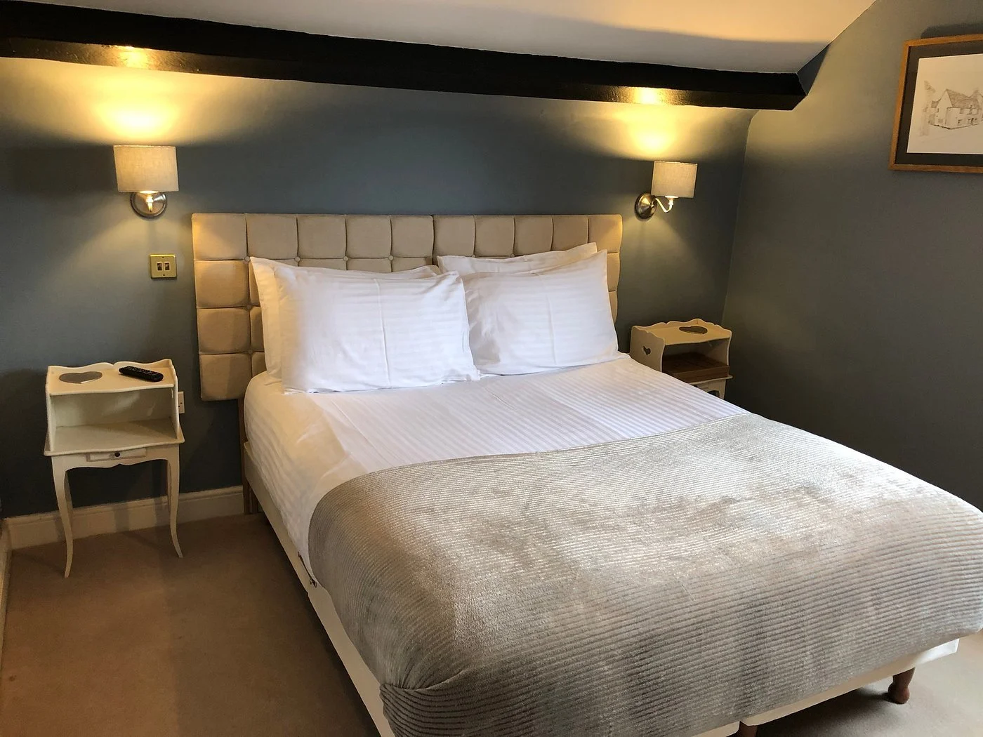 Our premium Loft Room at The Coachmakers Arms. A cozy bedroom featuring a bed with a padded beige headboard, white bedding, and two large pillows. This is a favoured room for Thames Walkers after a long day.