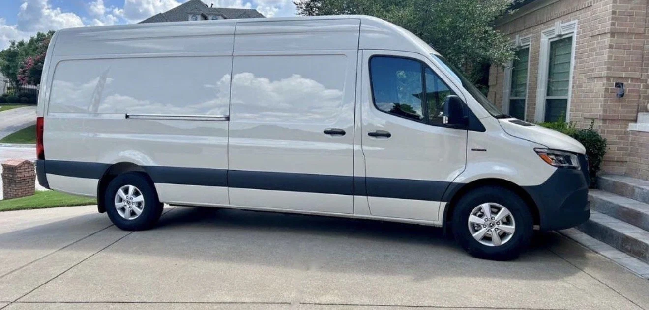 A white cargo van parked on a residential driveway next to a brick house with stairs leading to an entrance.