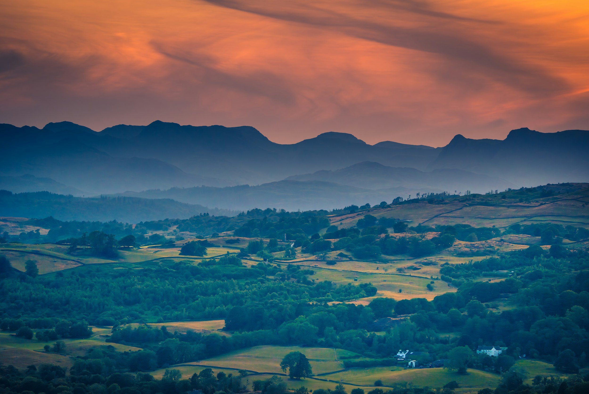 A scenic landscape of rolling green hills, distant mountains, and a colorful sunset sky with orange and pink clouds.