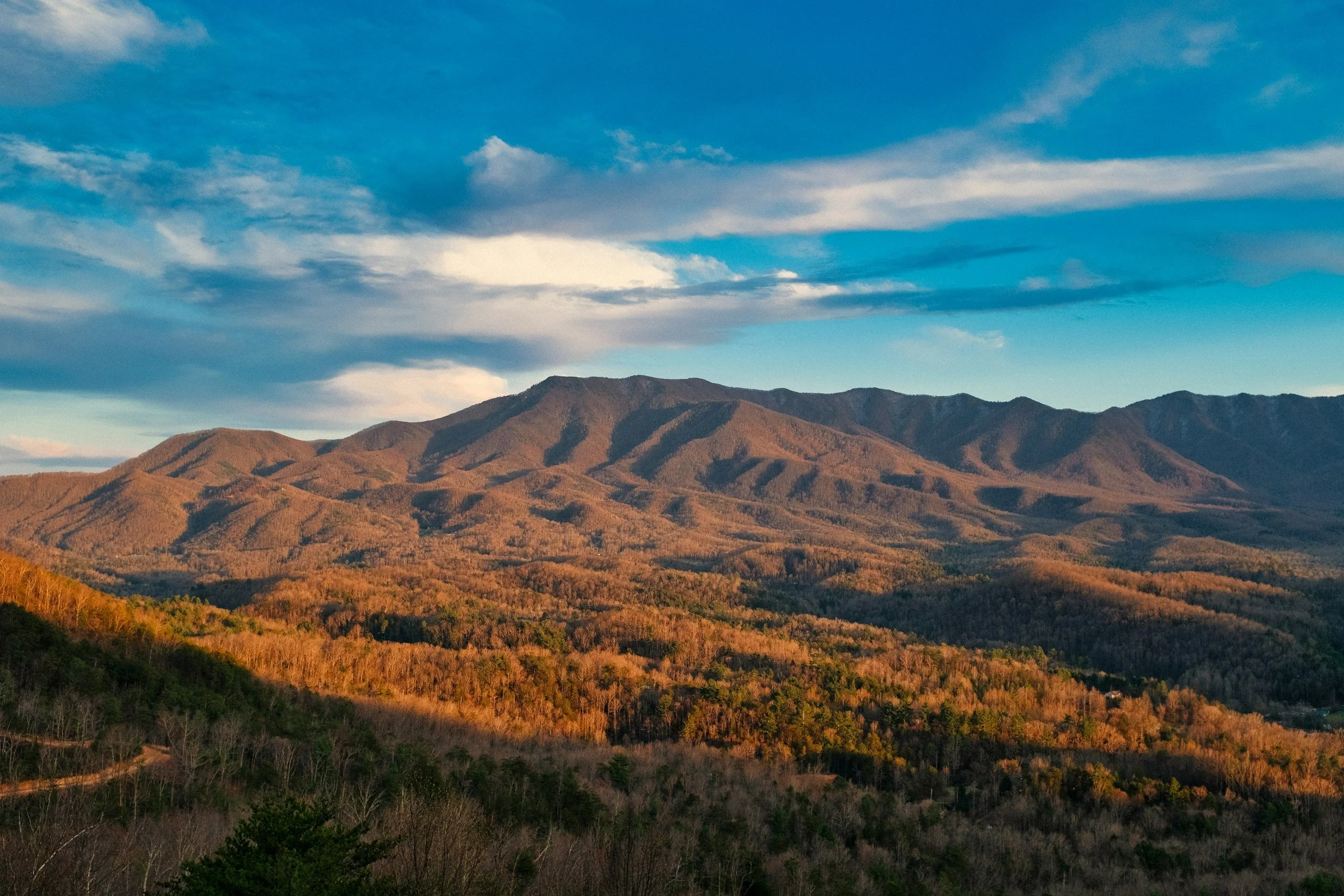 Scenic view of mountains with autumn-colored trees and a partly cloudy sky.
