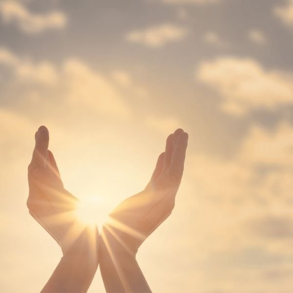 Two hands raised outward with the sun between them against a cloudy sky.