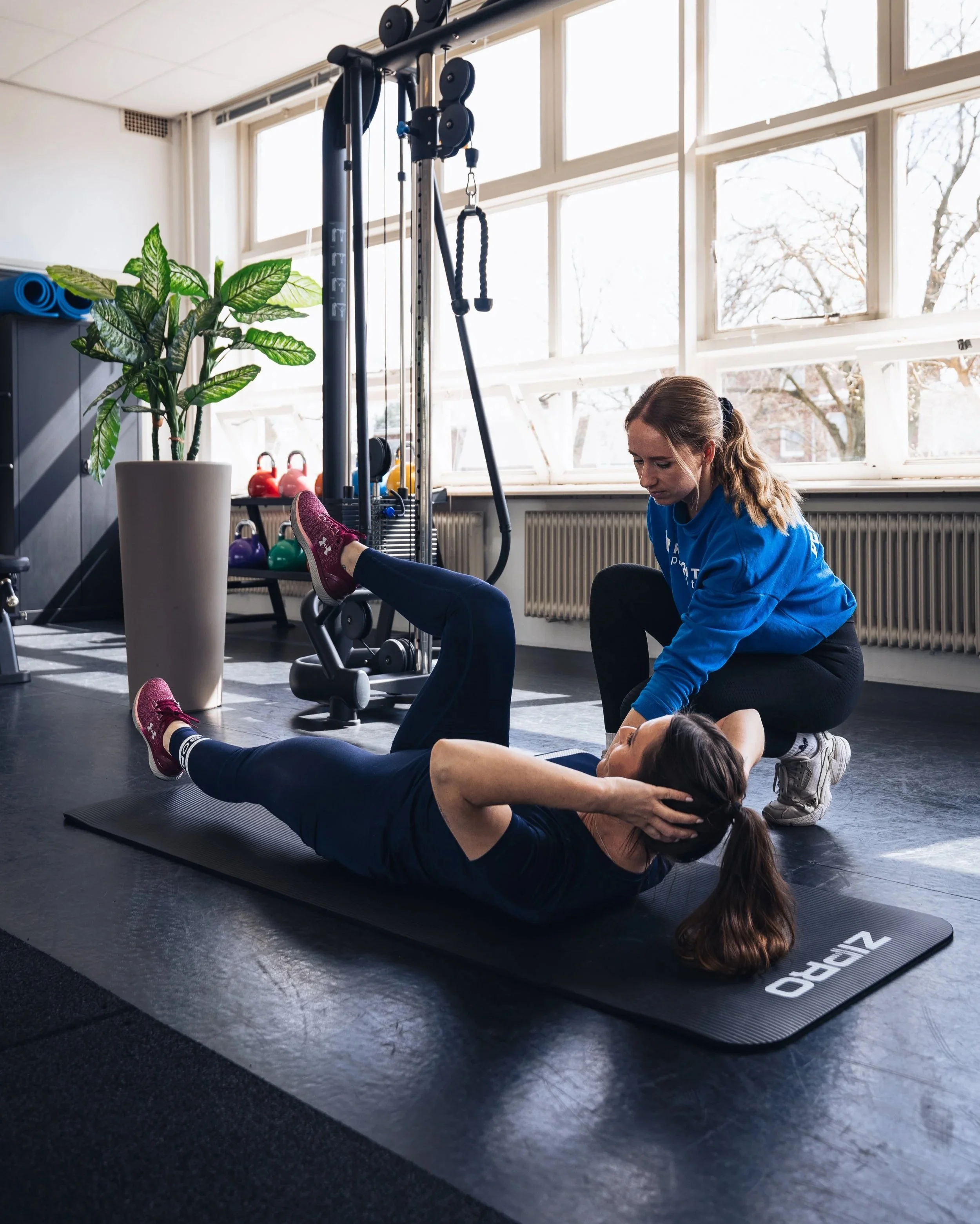 Vrouw die een buikspieroefening doet met begeleiding van een vrouwelijke personal trainer in een sportschool.