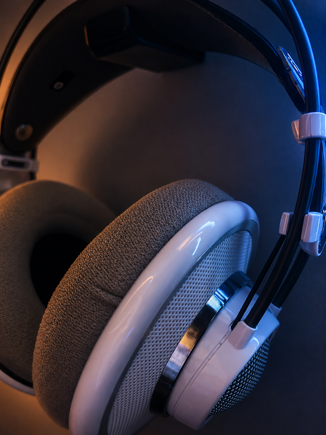 Close-up view of a pair of over-ear headphones with white and gray colors. The headphones are placed on a dark surface, with visible headband and ear cushions.