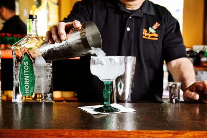 Bartender pouring a cocktail into a glass at a bar.