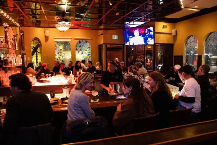 People dining at a bar in a restaurant with a TV screen on the wall.