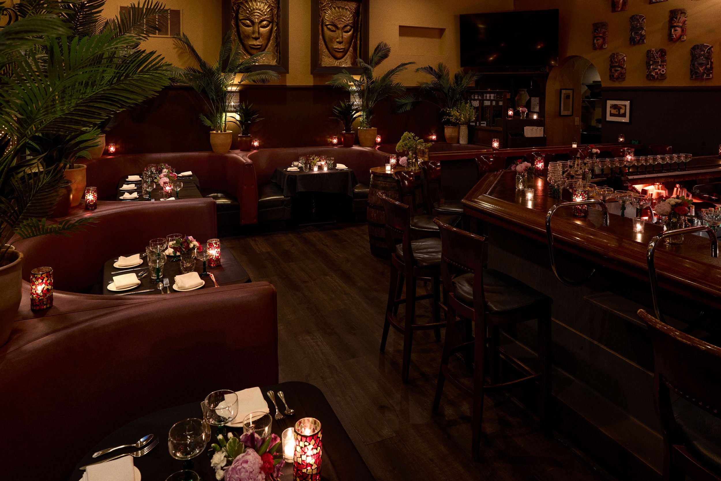 Dimly lit restaurant interior with plants, decorated tables, and artwork on the walls.