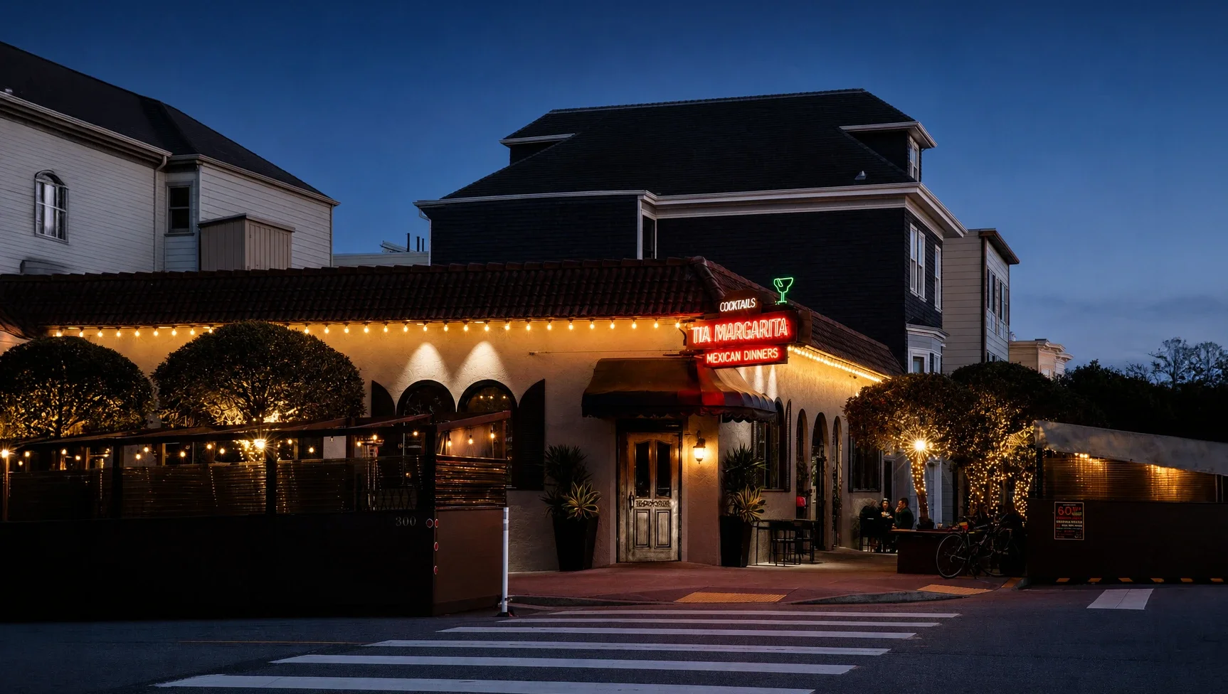 Night view of a restaurant with a red neon sign reading 'Tia Margarita Mexican Dinners,' illuminated windows, string lights, and trees decorated with fairy lights outside.
