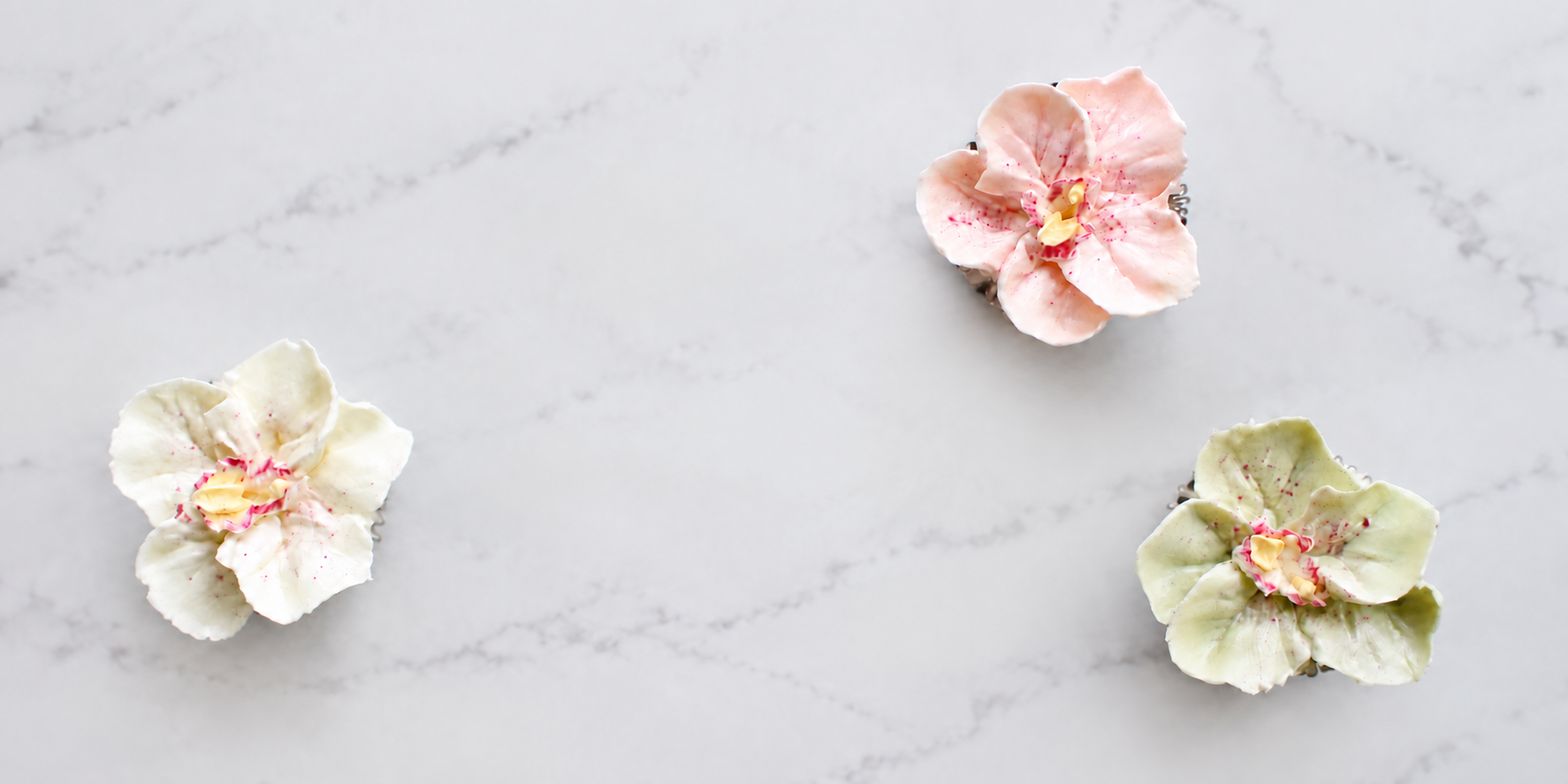 Three decorative sugar cookies shaped like flowers, with pink and white icing, on a white marble surface.