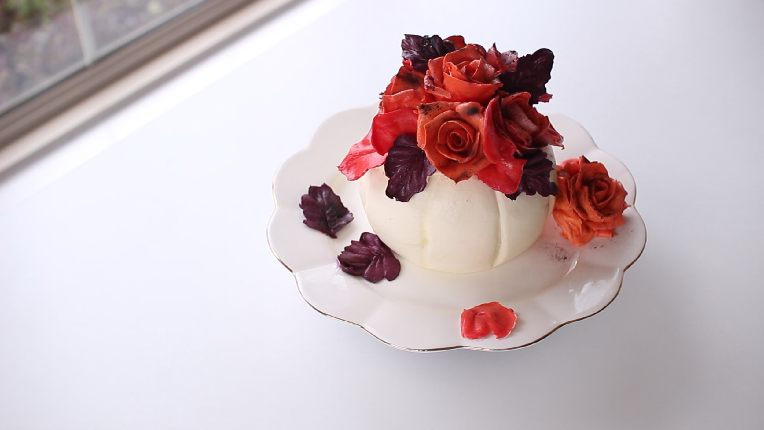 A white dessert topped with pink and dark purple flower-shaped garnishes on a decorative plate.