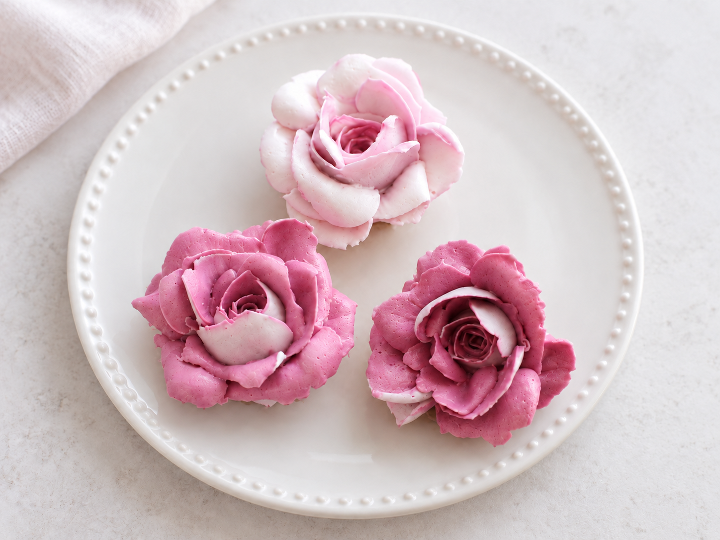 Three rose-shaped cookies in shades of pink and white on a white plate