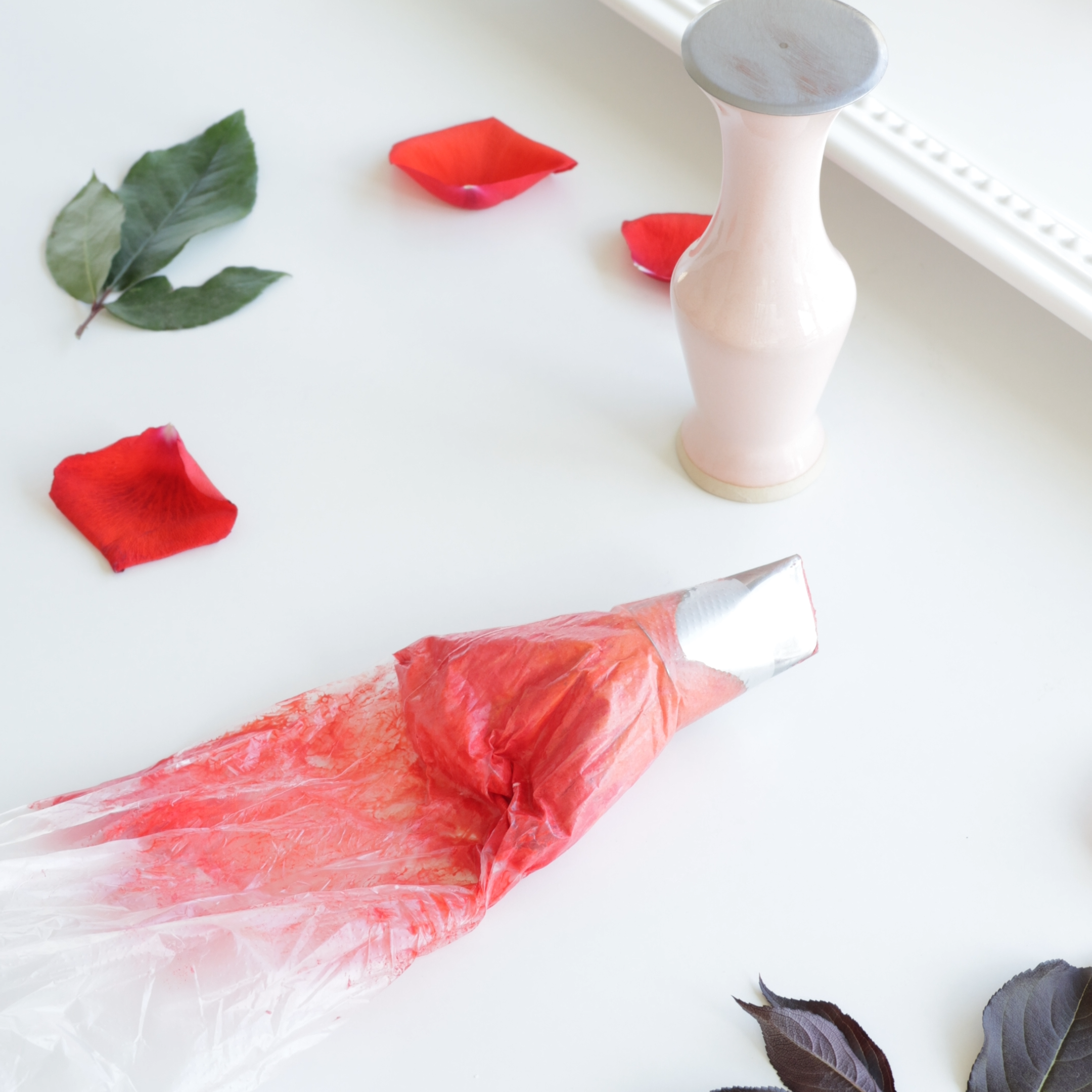 Pink paint in a tube with a pink wooden palette and dried rose petals and purple leaves on a white surface.