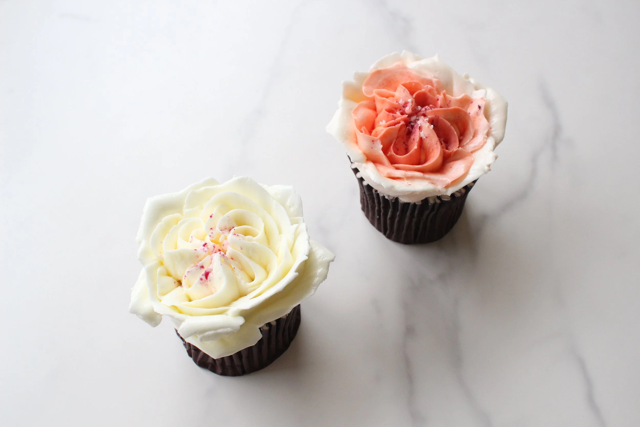 Three cupcakes with floral frosting designs on a white surface.