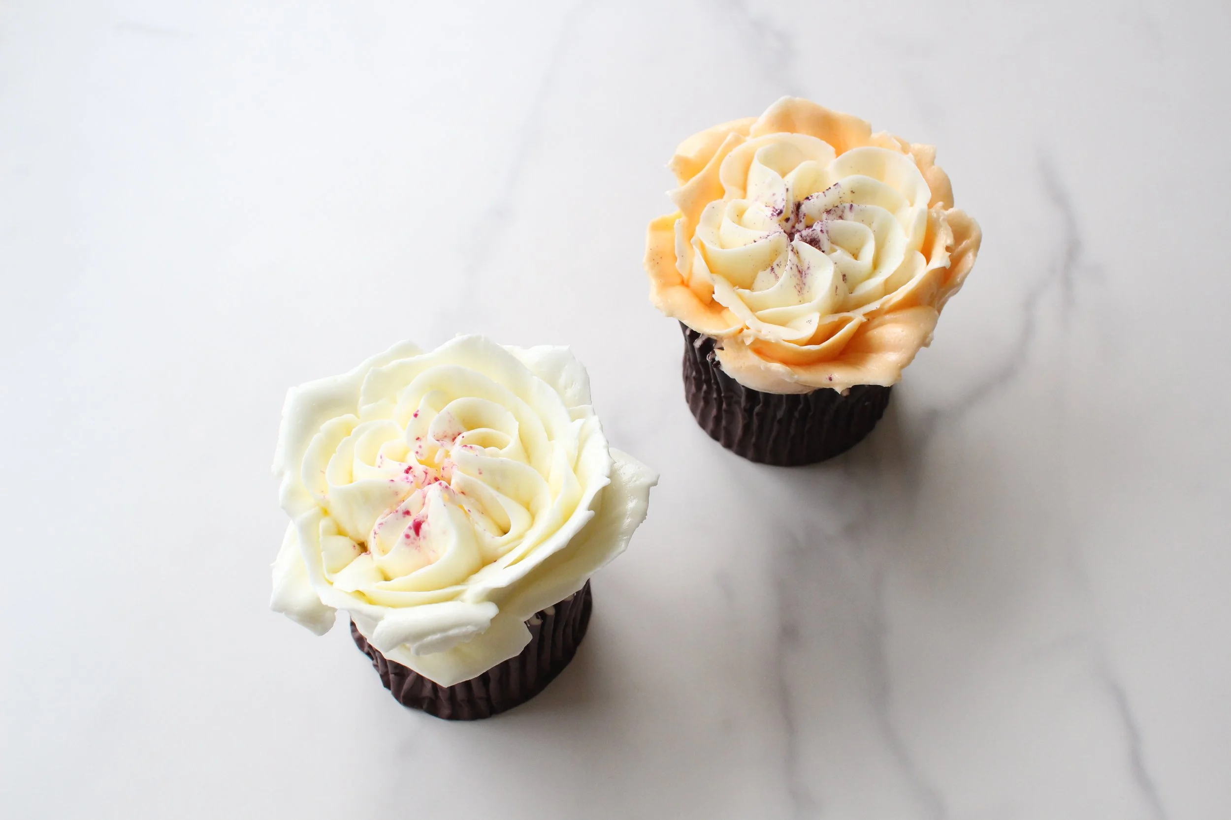 Three cupcakes decorated with white and light orange frosting shaped like roses, placed on a white surface.