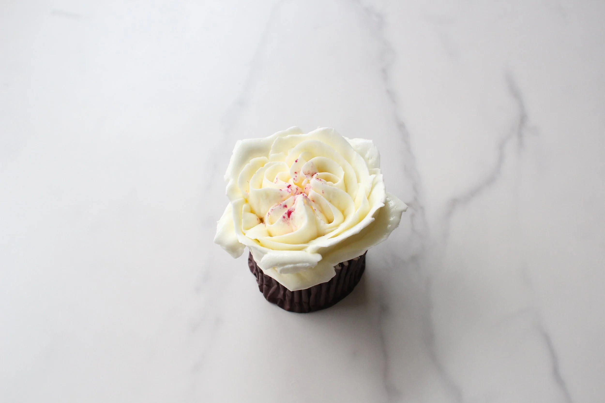 A cupcake with white frosting topped with pink sprinkles on a white surface.