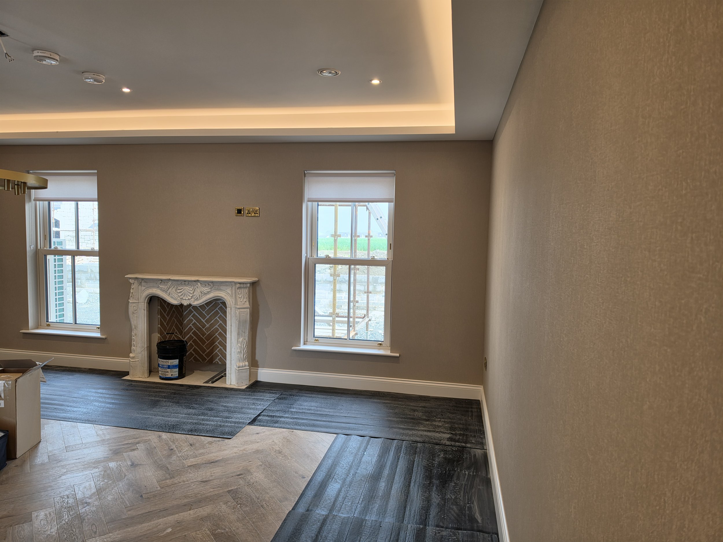 Interior of a room under renovation with a fireplace, multiple windows, and flooring in progress.