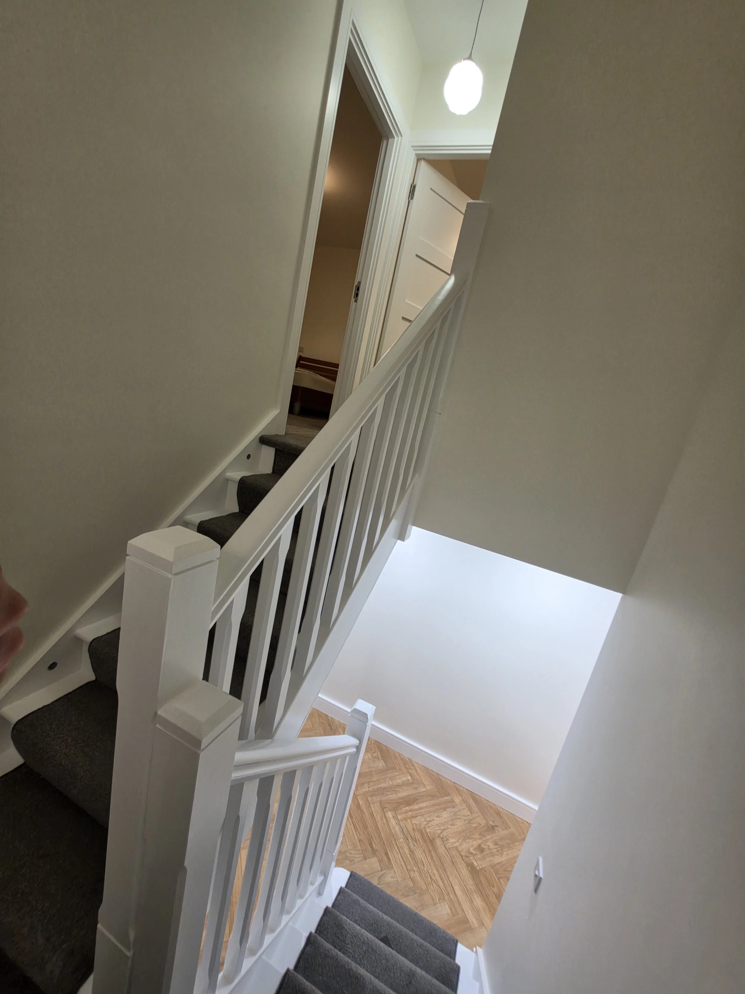 View of a staircase with dark carpeted steps, white railing, and beige walls leading to an upper floor with open doors and a light fixture hanging from the ceiling.