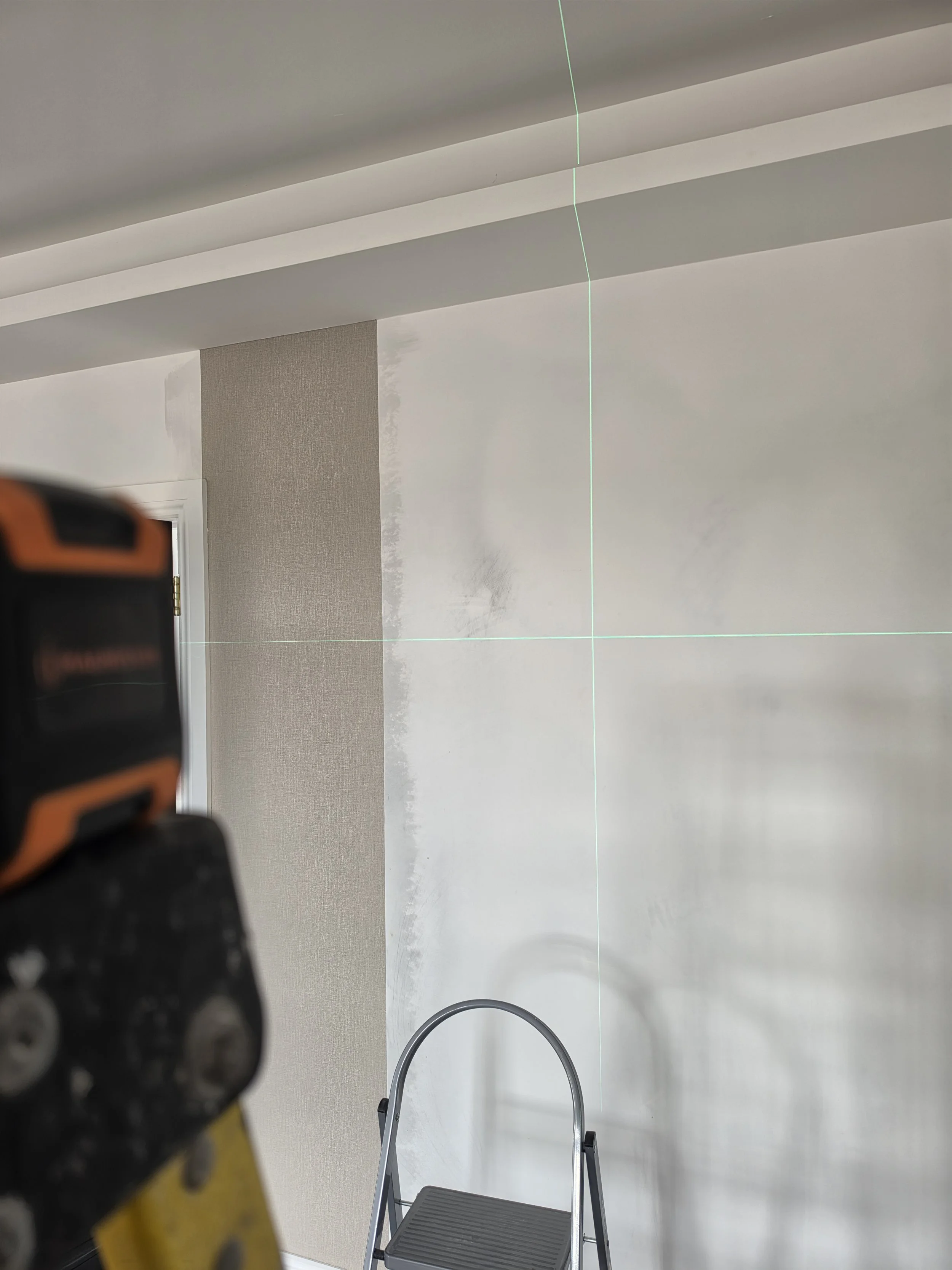 An empty room with gray walls, a white ceiling, and a gray ladder in the center. The photo is taken from under a ceiling vent, and part of an orange and black object is visible in the foreground.