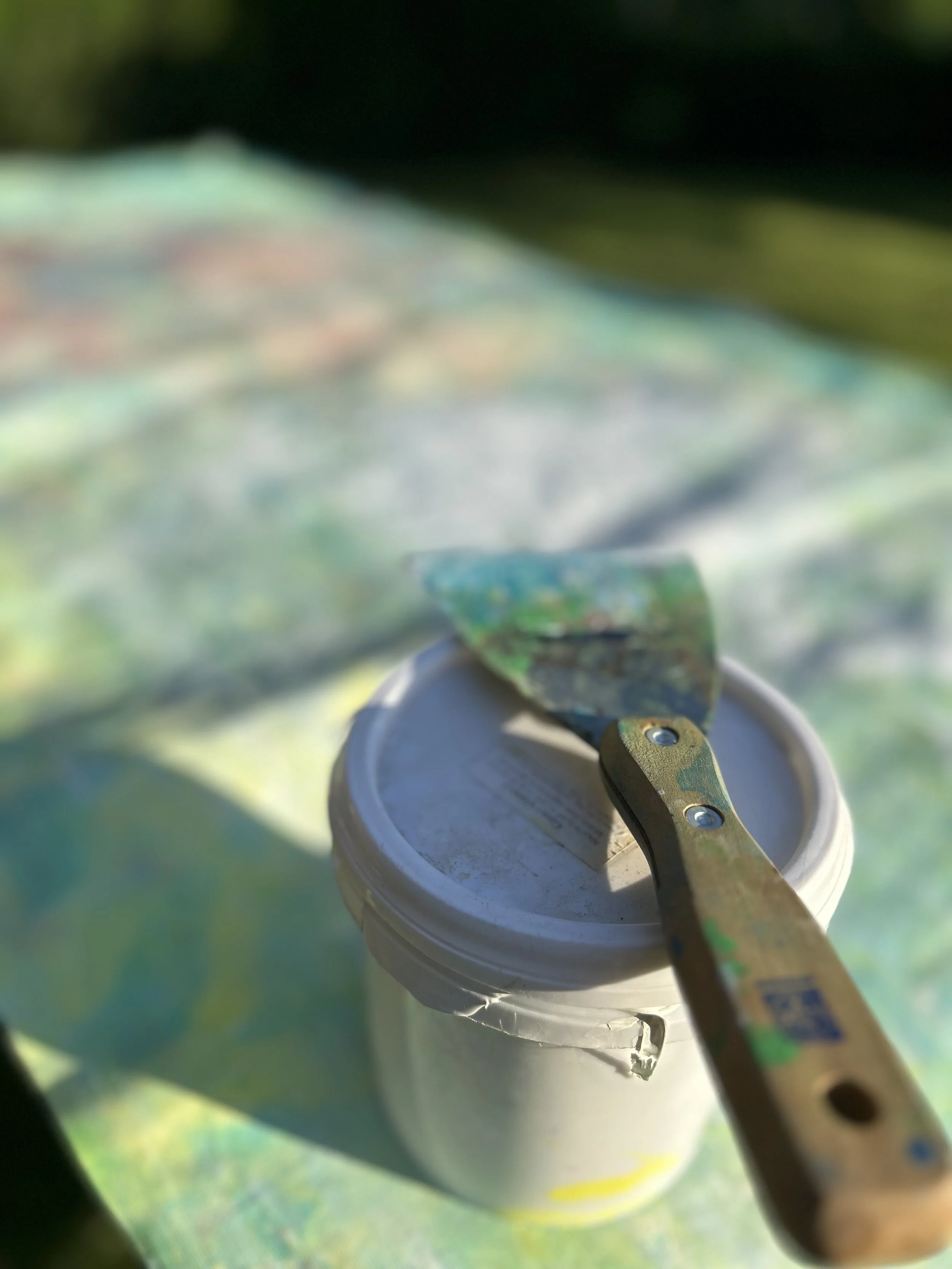 A paint can with an open lid, a paintbrush inserted into the can, and a blurred green background.