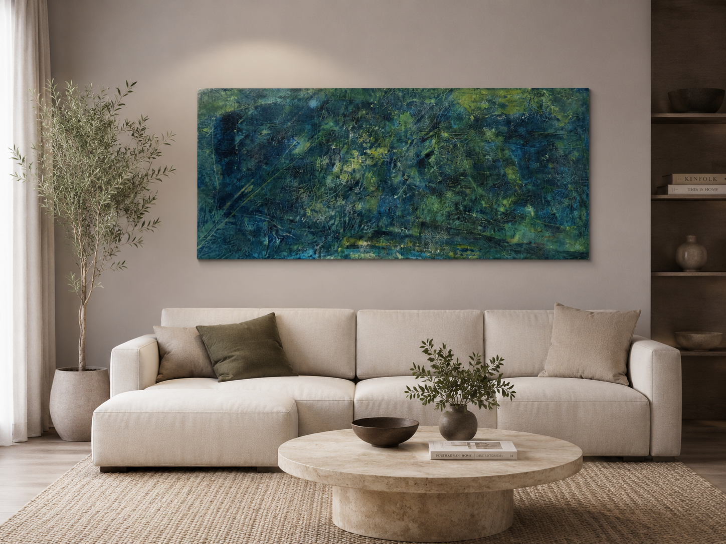 Living room with a white sofa, green and beige pillows, a round beige coffee table with a plant in a gray vase and a book, a tall potted plant, a large abstract painting with green, blue, and dark colors on the wall, and built-in shelves with books and vases.