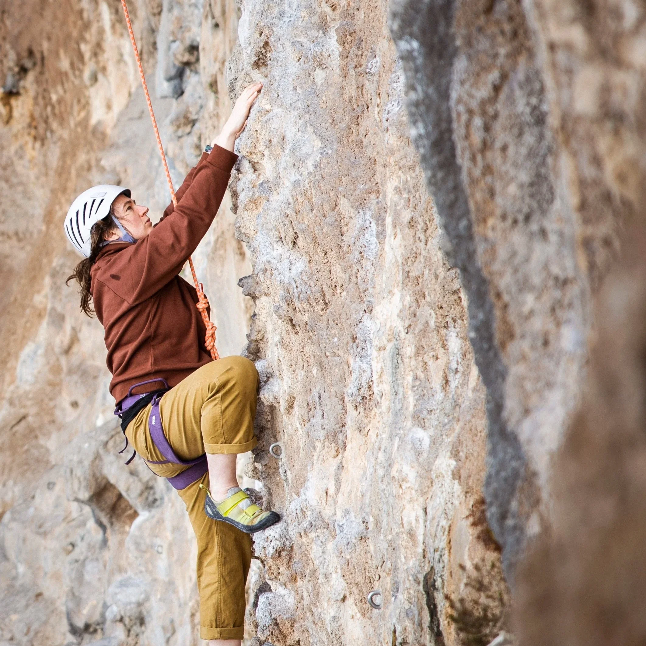 A person wearing a helmet and climbing gear, ascending a steep rock face with safety harnesses.