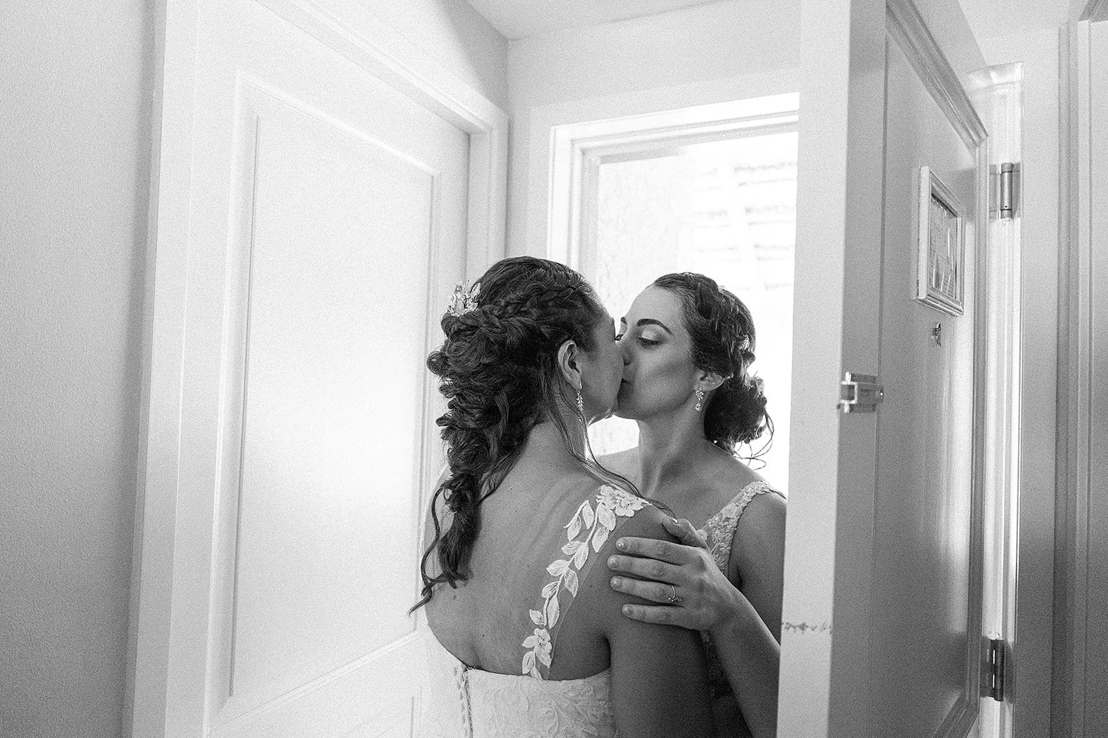 Dos mujeres, probablemente novias, compartiendo un beso en una habitación con luz natural