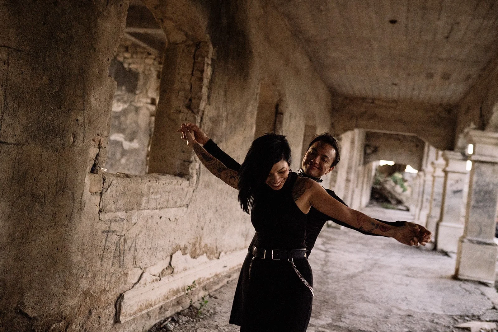 Dos personas bailando en un pasillo de un edificio antiguo, con paredes de piedra y ventanas abiertas.