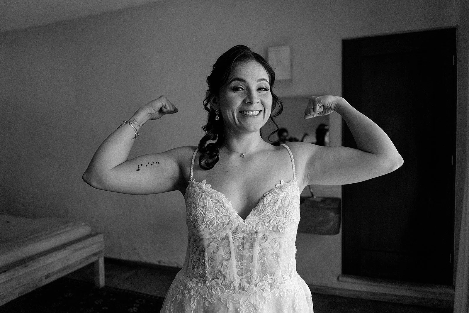 Mujer con vestido de novia, sonriendo y mostrando sus músculos en una pose de fuerza en una habitación.