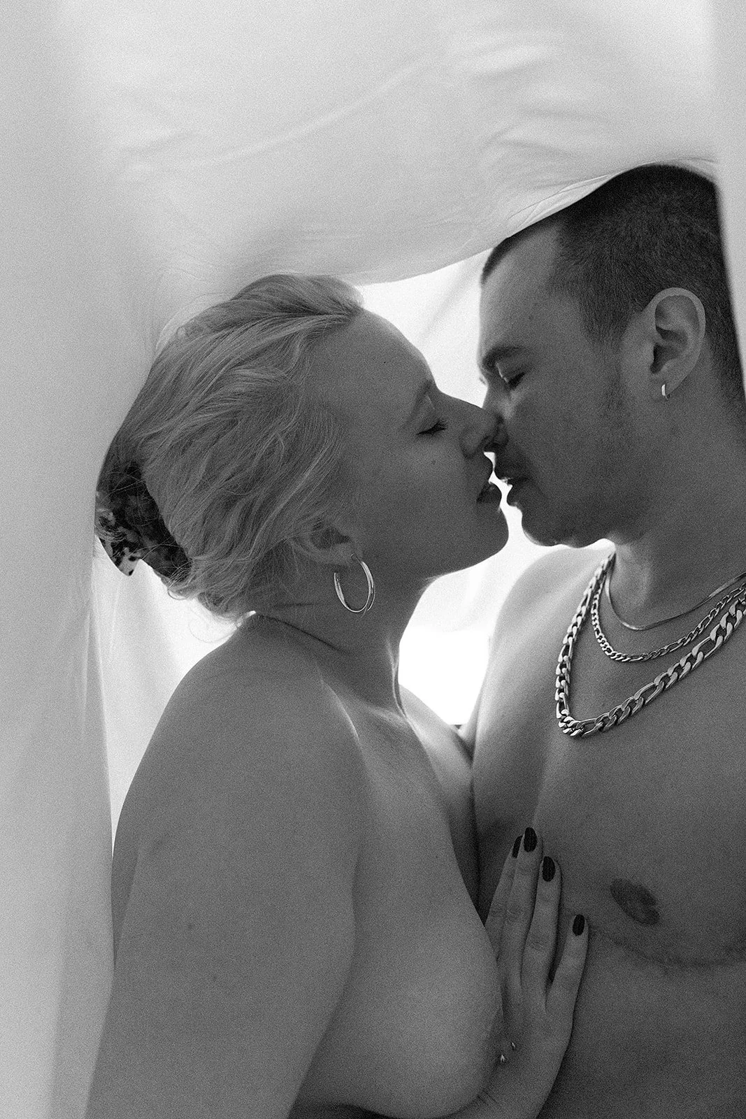 Una pareja desnuda en una pose íntima, casi besándose, en un entorno con luz natural.